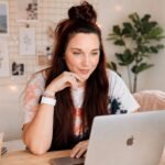 Business owner researching Pinterest keywords on a laptop before designing a Pin, with a notebook and coffee nearby.