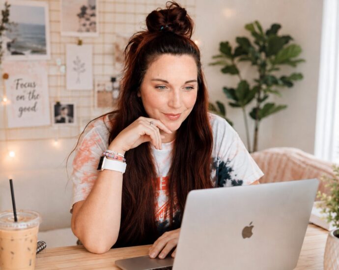 Business owner researching Pinterest keywords on a laptop before designing a Pin, with a notebook and coffee nearby.