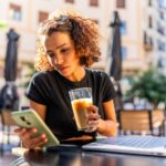 Content creator looking at her phone while working at a coffee shop.